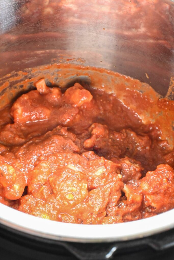 A red sauce inside of an instant pot, with chunks of cauliflower seen