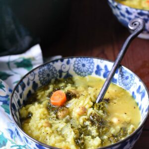 a blue and white flowered bowl filled with greek lemon and rice soup, with carrots, kale and chickpeas visible in the soup. There is another bowl in the background, and they are on a dark wooden surface