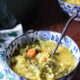 a blue and white flowered bowl filled with greek lemon and rice soup, with carrots, kale and chickpeas visible in the soup. There is another bowl in the background, and they are on a dark wooden surface