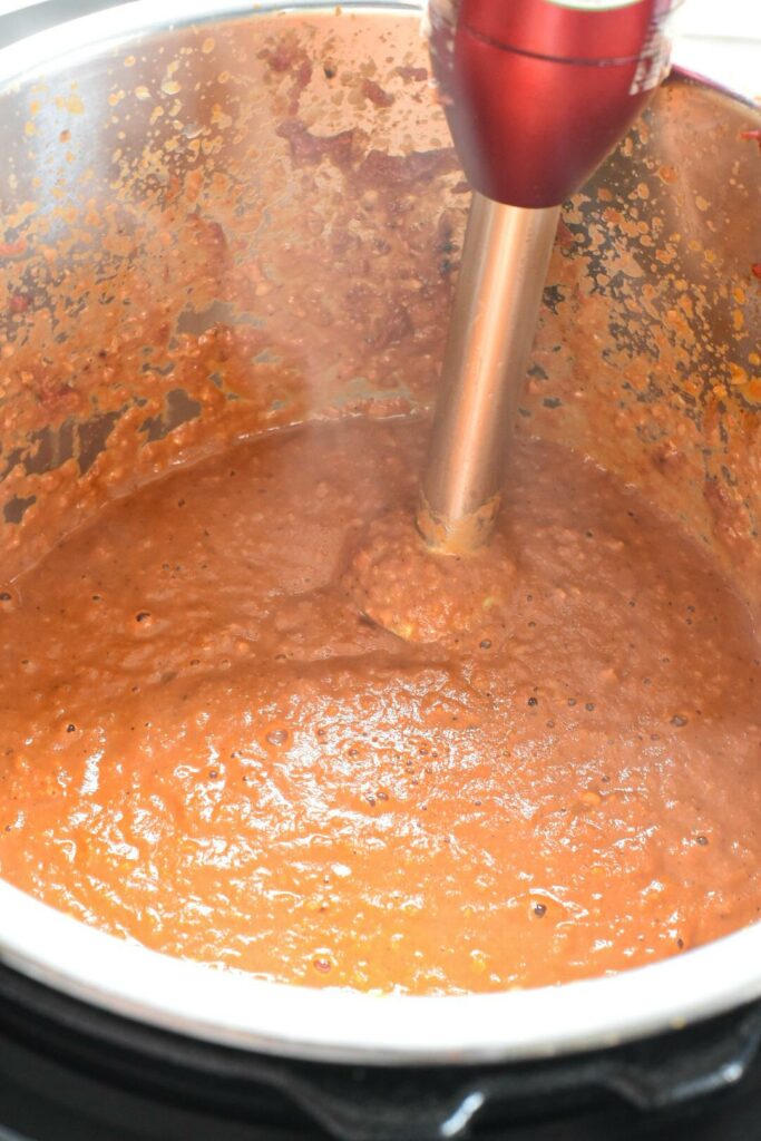 A blended red curry inside of an instant pot, with a hand held blender in the image