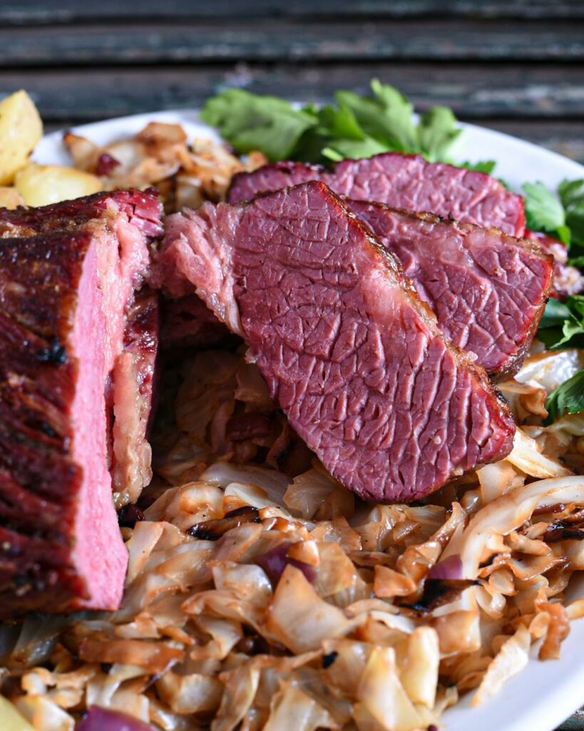 A close up of sliced crispy corned beef on top of a bed of lemony cabbage and potatoes.
