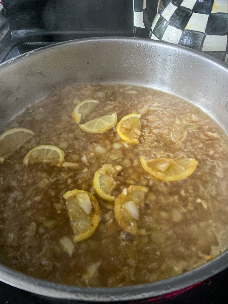 Lemon butter sauce for chicken sizzling in a skillet with lemon rinds.