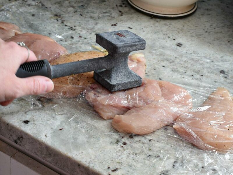 easy chicken piccata recipe A hand holding a poultry hammer pounding chicken breasts in between two pieces of plastic wrap
