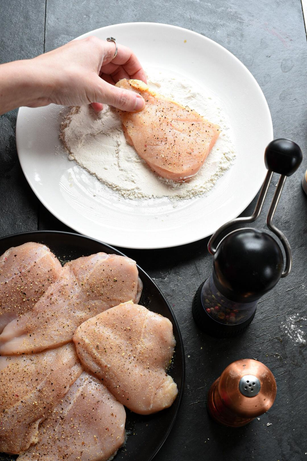Dredging chicken breasts through white all purpose flour for lemon chicken piccata
