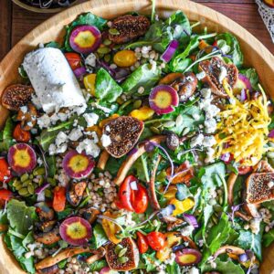 A large wooden serving bowl filled with mushroom and kale winter salad, topped with figs and goat cheese