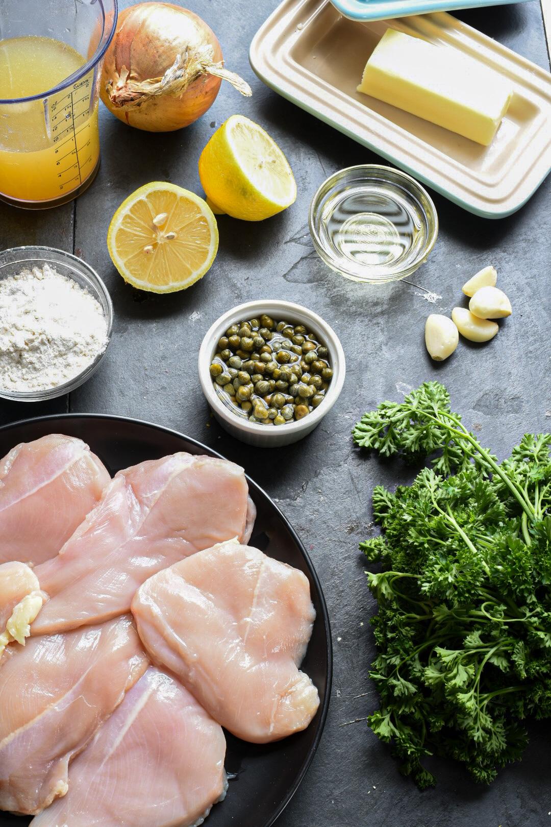 An overhead shot of the ingredients needed to make easy chicken piccata including capers chicken breasts and lemons.