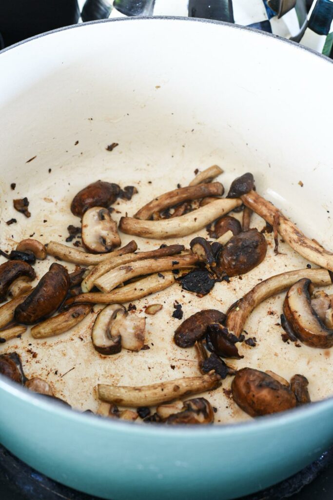 Shiitake mushrooms being sauteed in a blue Le Creuset dutch oven