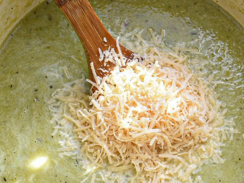 Green asparagus soup in a large pot blended with a handful of shredded parmesan on top