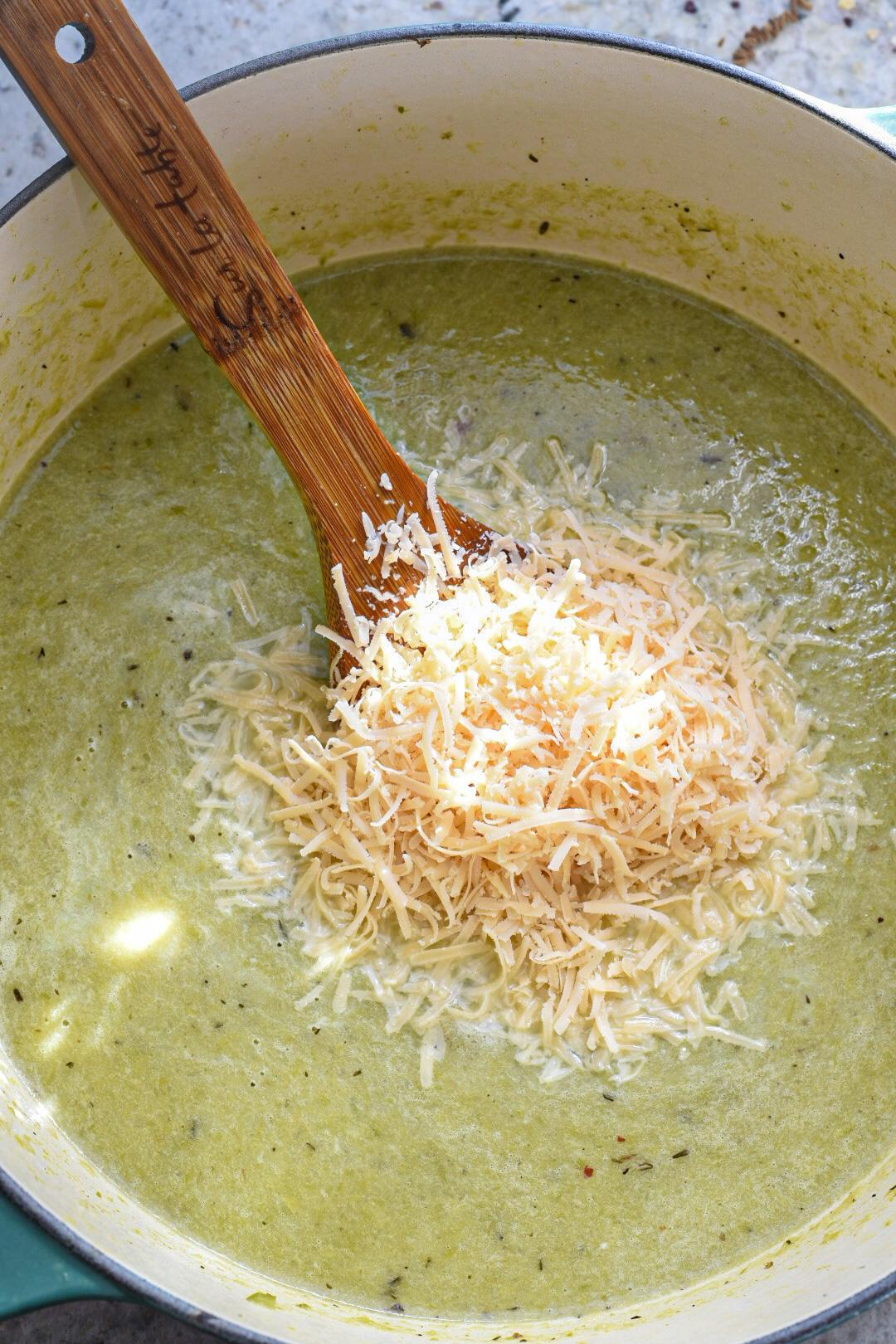 Green asparagus soup in a large pot blended with a handful of shredded parmesan on top