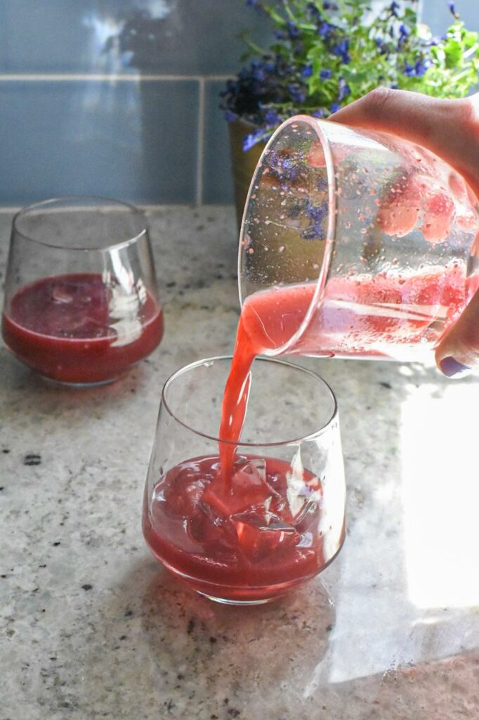 A fruity gin cocktail being poured into a glass with ice.