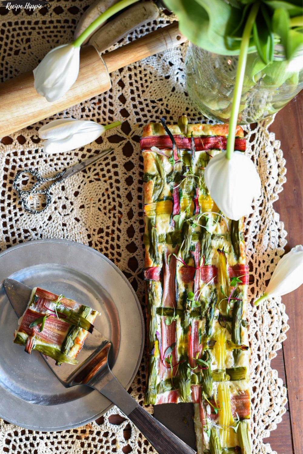 A vegetable lattice puff pastry tart with woven vegetables and egg whites on a lace table runner.