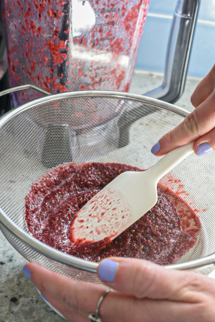 Blended up cucumber and blackberries in a strainer being pressed down