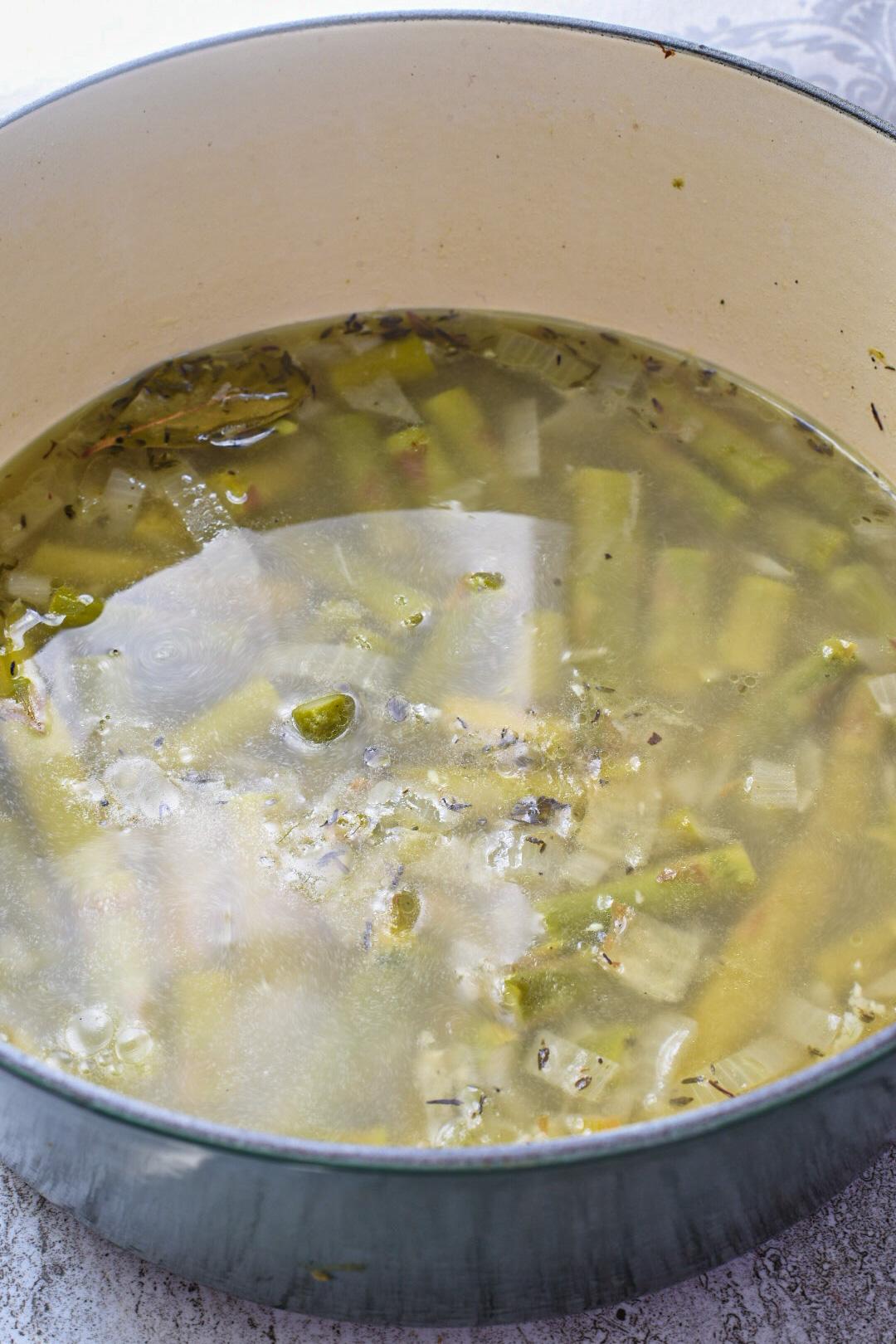 Asparagus in a large pot with broth over it being cooked for no milk asparagus soup.