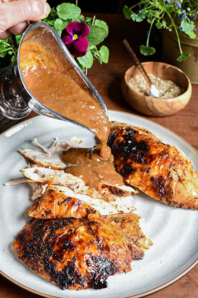 Jerk gravy being poured out of a silver gravy dish over cooked skin on turkey breasts.