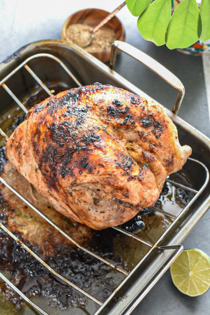A fully cooked jamaican jerk turkey breast on a turkey rack with a wire.