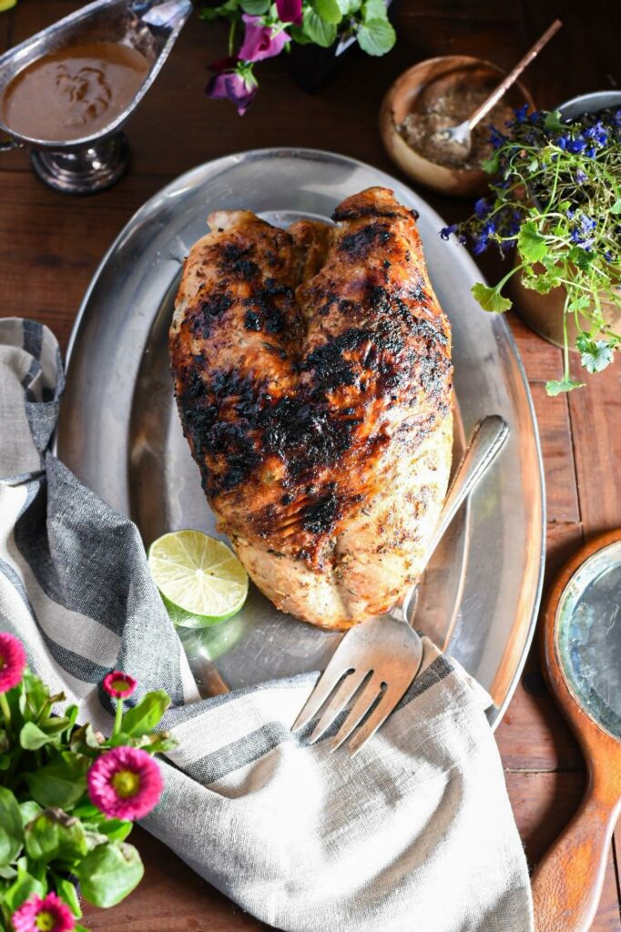 A jamaican jerk turkey breast on a silver serving platter surrounded by pink and purple flowers.