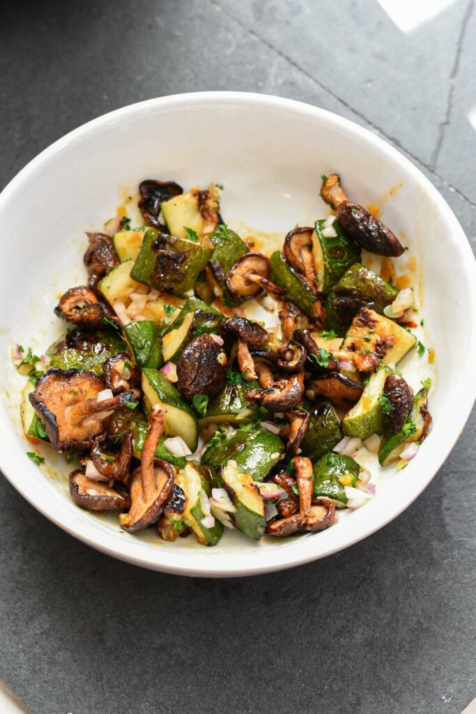 A bowl filled with grilled shiitake mushrooms and zucchini in a sauce