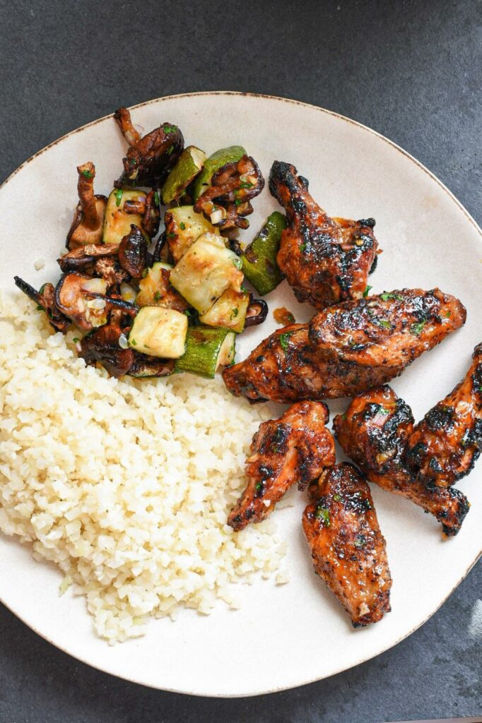 A plate with cauliflower rice, grilled chicken wings and grilled veggies