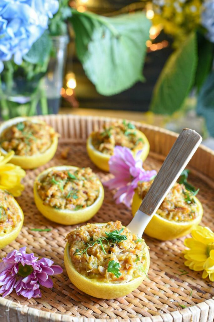 Stuffed lemon crab cakes on a wicker serving tray with purple flowers on the tray and blue flowers in the background. There is a small spoon coming out of the first crab cake