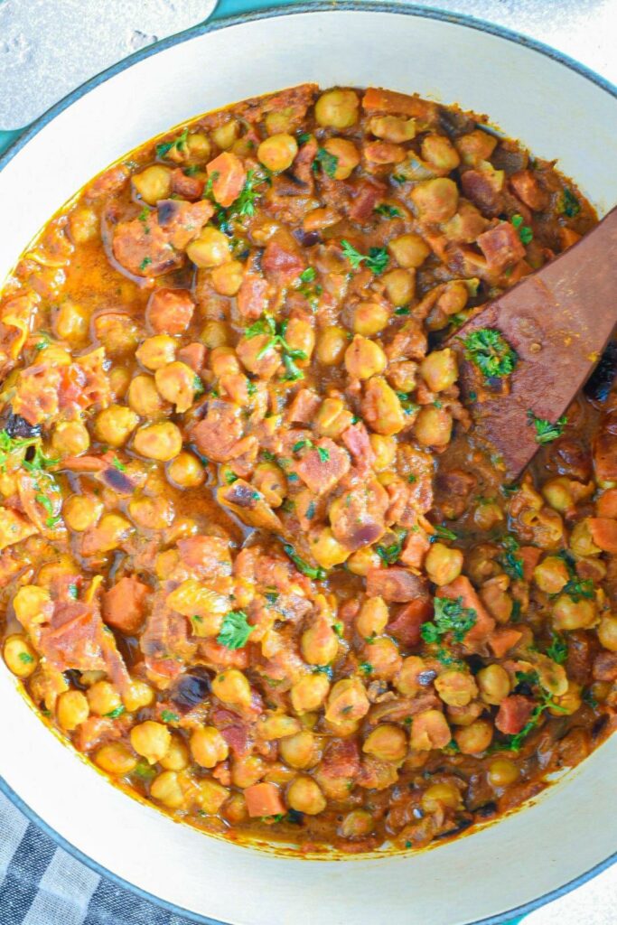 A large dutch oven filled with curried chickpeas and sprinkled with parsley.