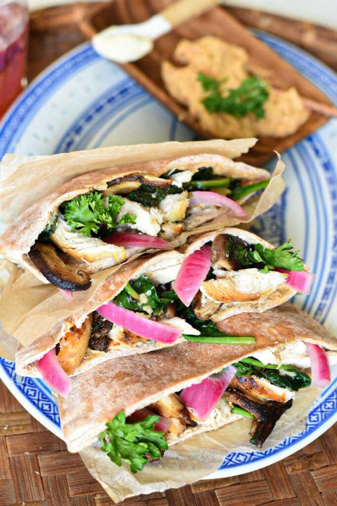 Three stuffed pita sandwiches with red onion, spinach, chicken and sauce visible on a blue serving platter.