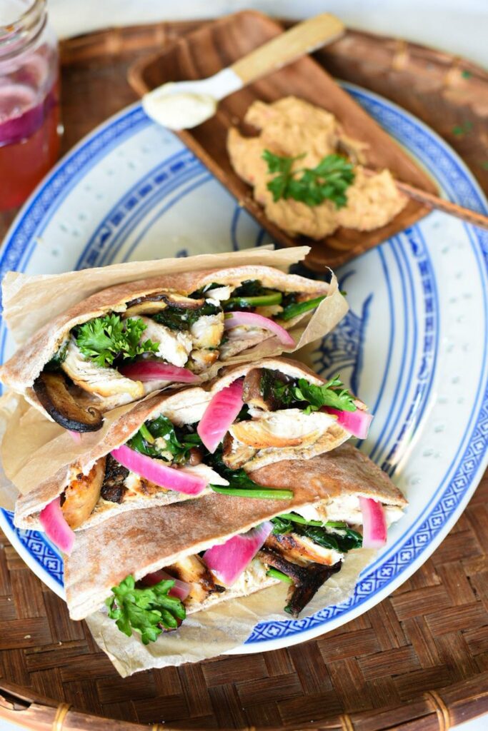 three chicken pita sandwiches filled with greens, pickled red onions and chicken on a blue serving platter.