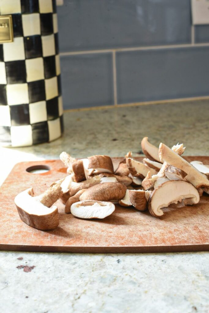 a cutting board on a counter with shiitake mushrooms on it and blue subway tiles behind it.