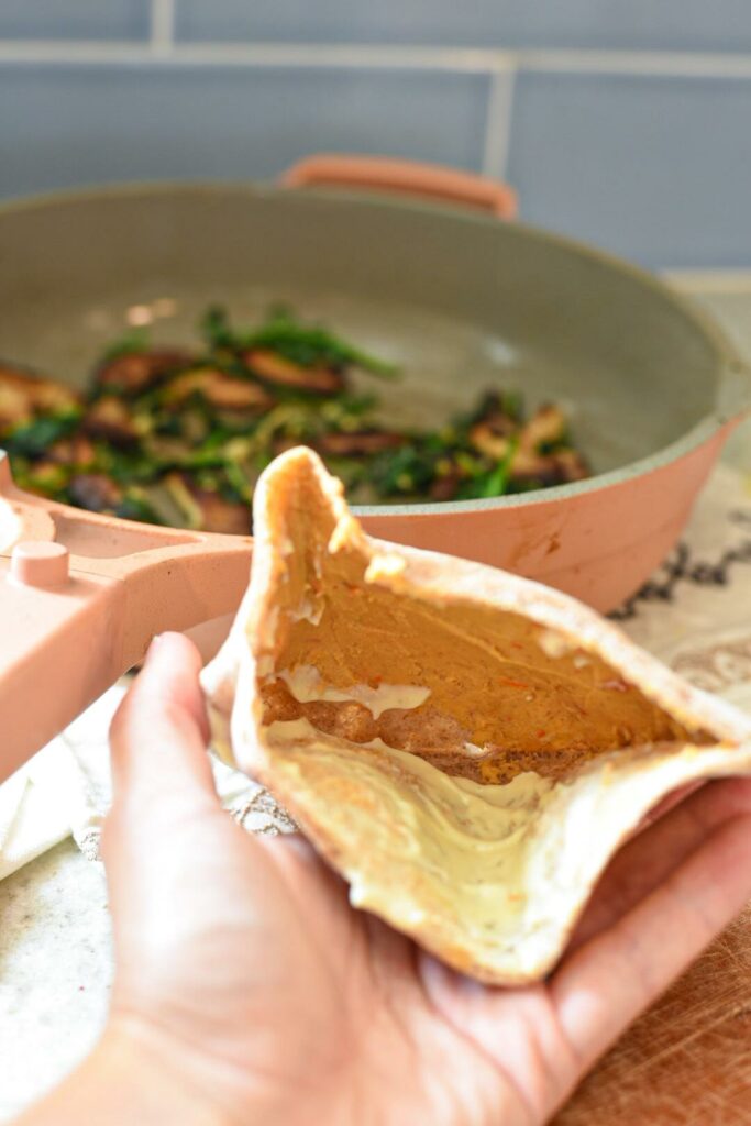 A hand holding an open pita pocket with hummus inside of it.