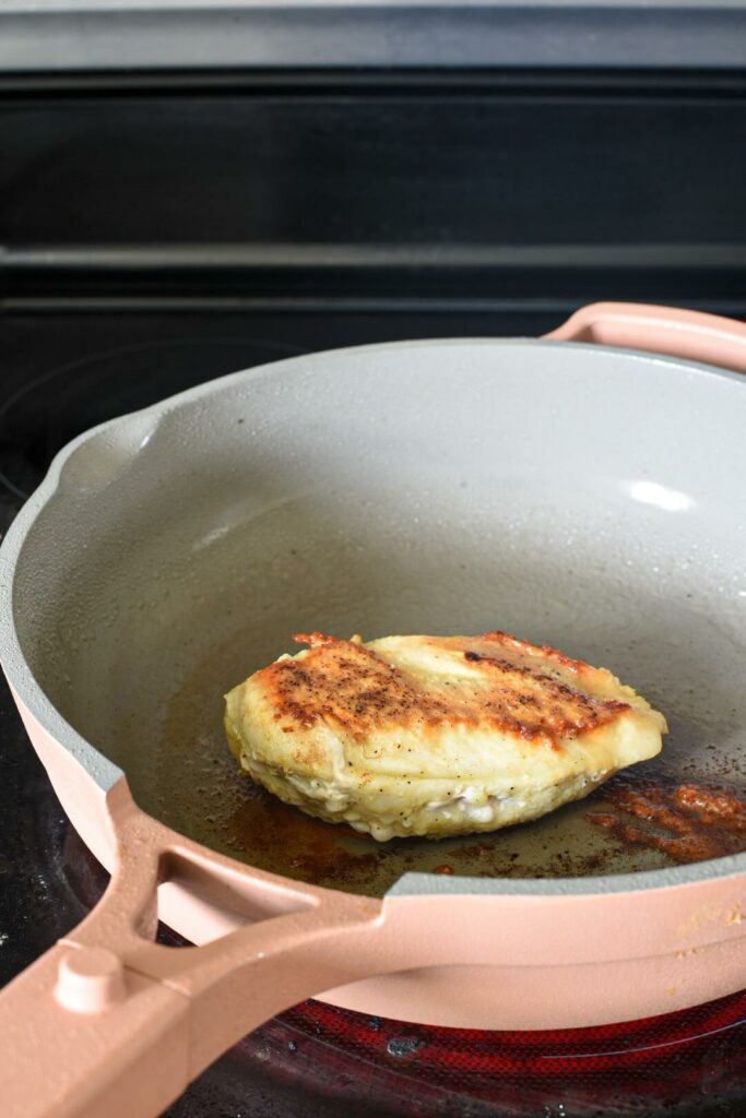 A large chicken breast in a pink pan on the stove top with a golden top.