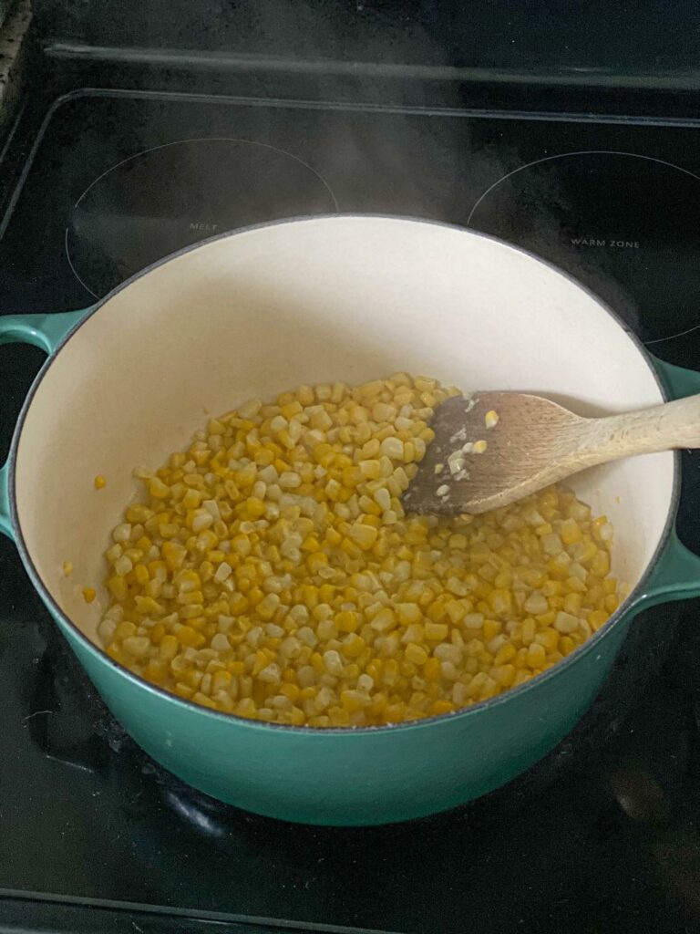 Corn kernels cooking in butter in a large blue dutch oven on an electric stove