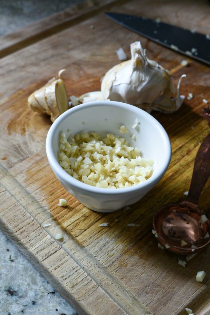 A small bowl filled with chopped fresh ginger and garlic on a wooden cutting board.