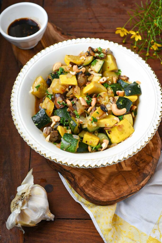 A vintage bowl filled with sauteed zucchini and squash and mushroom and onion on a wooden surface.