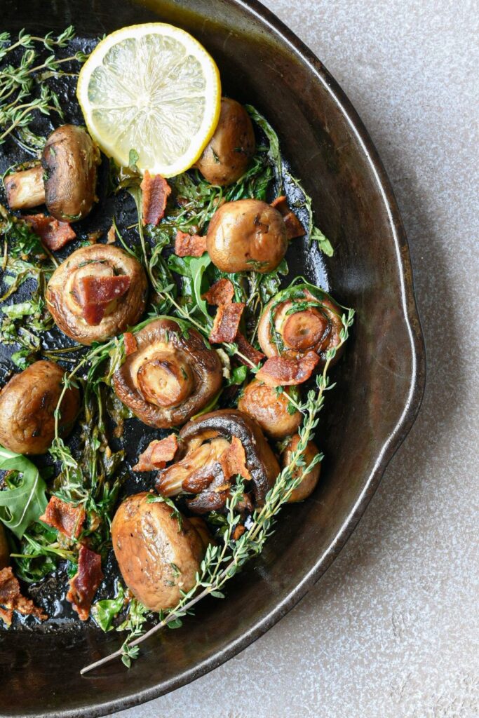 sauteed baby bella mushrooms in a black cast iron skillet topped with thyme sprigs and bacon