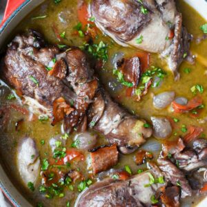 An overhead shot of chicken in red wine sauce with whole drumsticks and bacon.