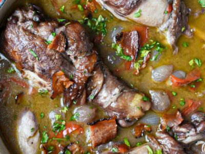 An overhead shot of chicken in red wine sauce with whole drumsticks and bacon.