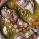 An overhead shot of chicken in red wine sauce with whole drumsticks and bacon.