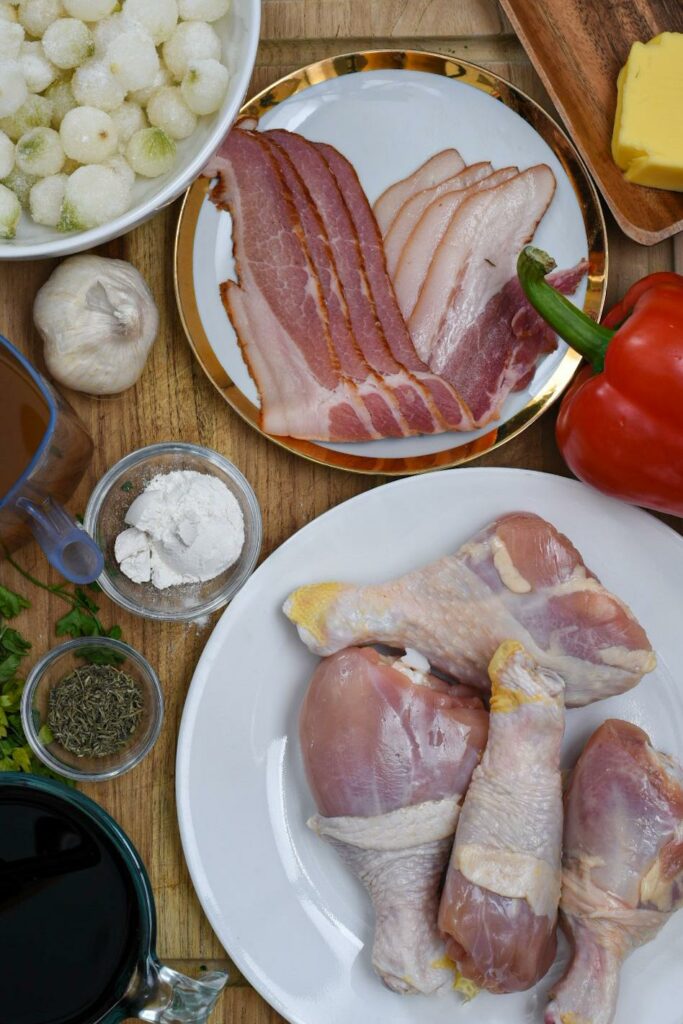 Overhead shot of coq au vin ingredients like raw chicken drumsticks, spices, broth and bacon.