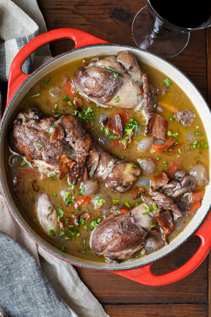 An overhead shot of coq au vin without cognac with whole chicken drumsticks in a red dutch oven