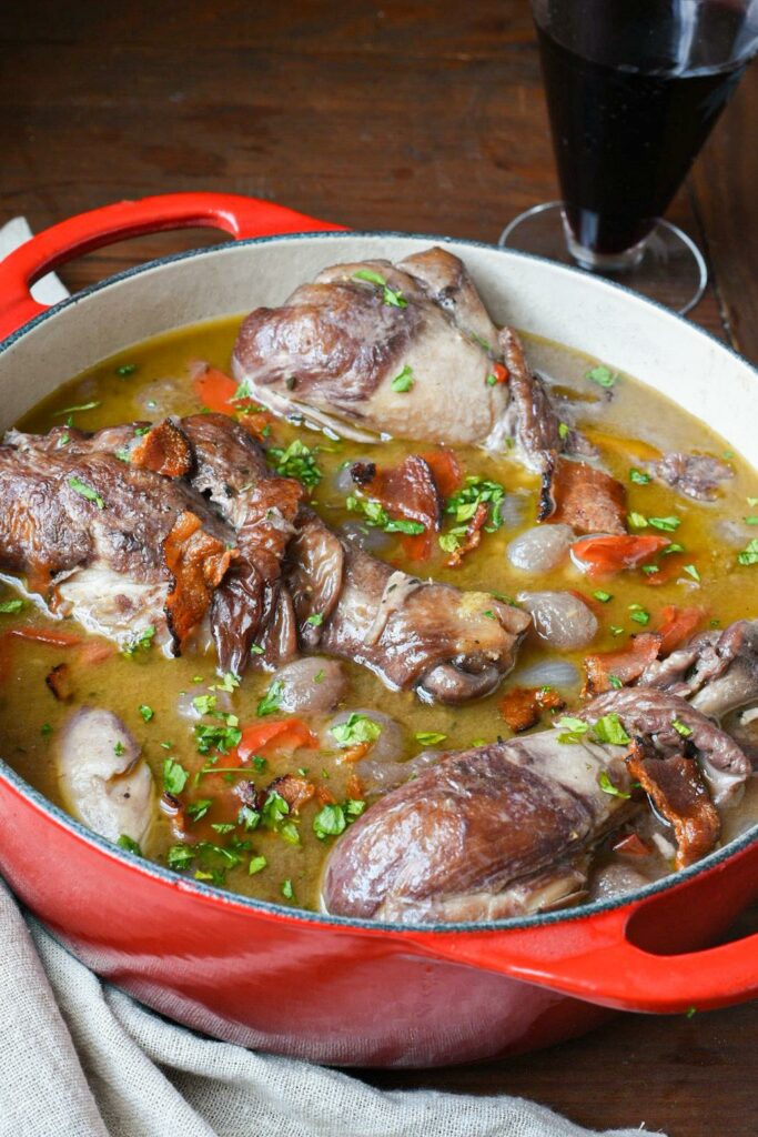 Close up image of braised chicken drumsticks in a one pot coq au vin recipe inside of a red dutch oven.