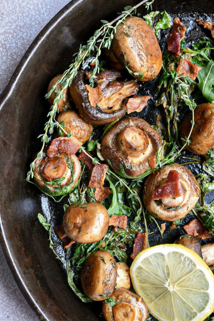 baby bella mushrooms in a cast iron skillet with arugula and bacon