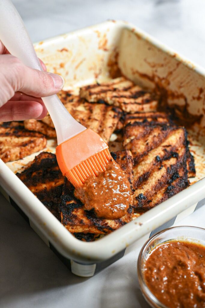 grilled tofu being marinaded with a chipotle sauce on a brush