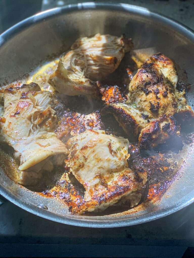 A skillet with pan seared chicken thighs that are browning.