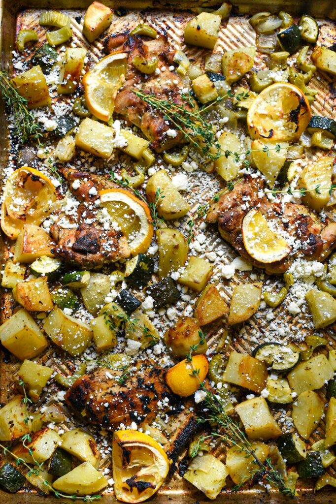 Greek sheet pan chicken thighs and vegetables, with charred lemon rinds, sprinkled feta cheese and thyme sprigs.
