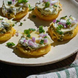 Crispy polenta cakes topped with hummus, tzatziki, red onion and green scallions