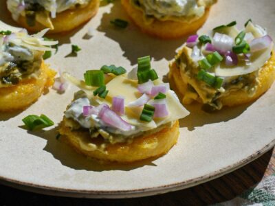 Crispy polenta cakes topped with hummus, tzatziki, red onion and green scallions