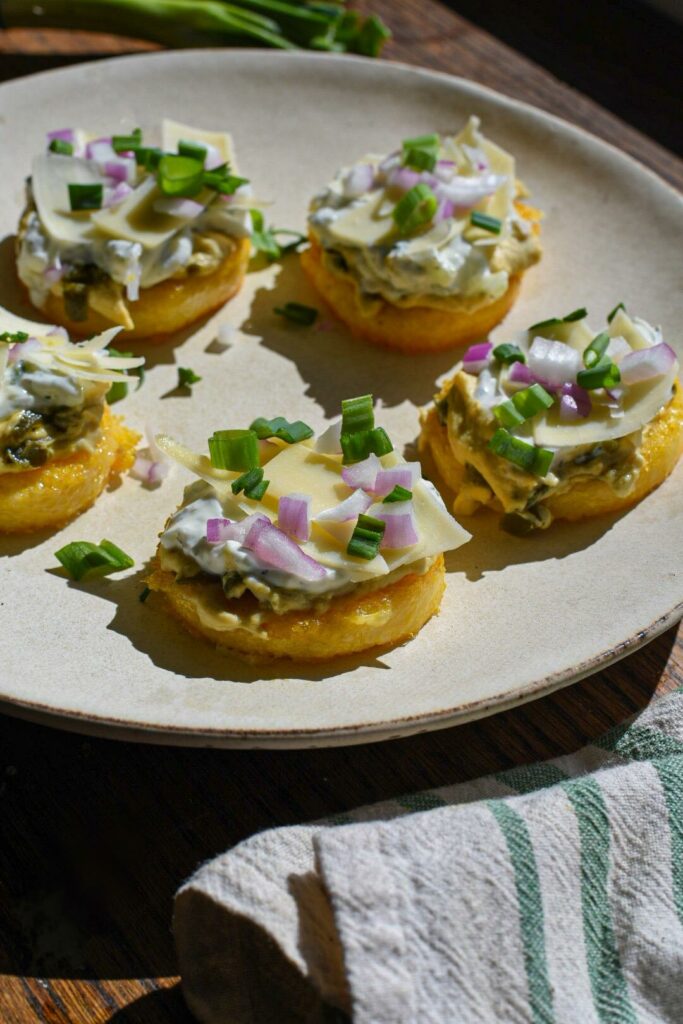 Crispy polenta cakes topped with hummus, tzatziki, red onion and green scallions