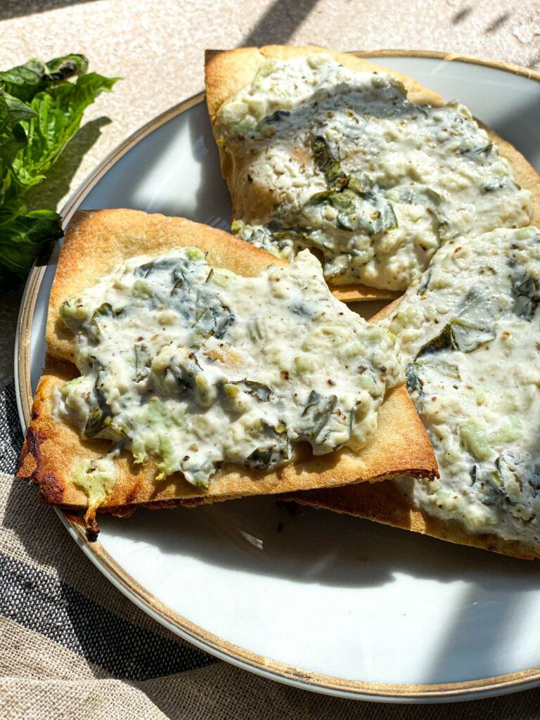 a close up shot of baked pita triangles topped with a white feta and greek yogurt sauce