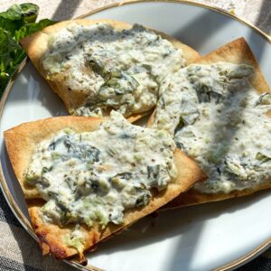 a gold rimmed appetizer plate with three triangular slices of baked crispy pita bread, topped with feta and greek yogurt.