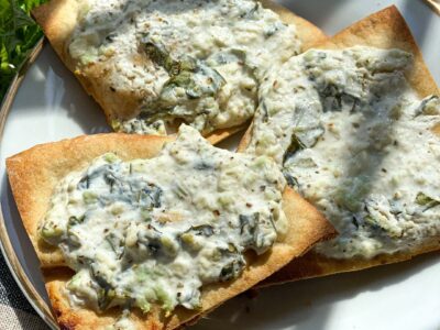 a gold rimmed appetizer plate with three triangular slices of baked crispy pita bread, topped with feta and greek yogurt.
