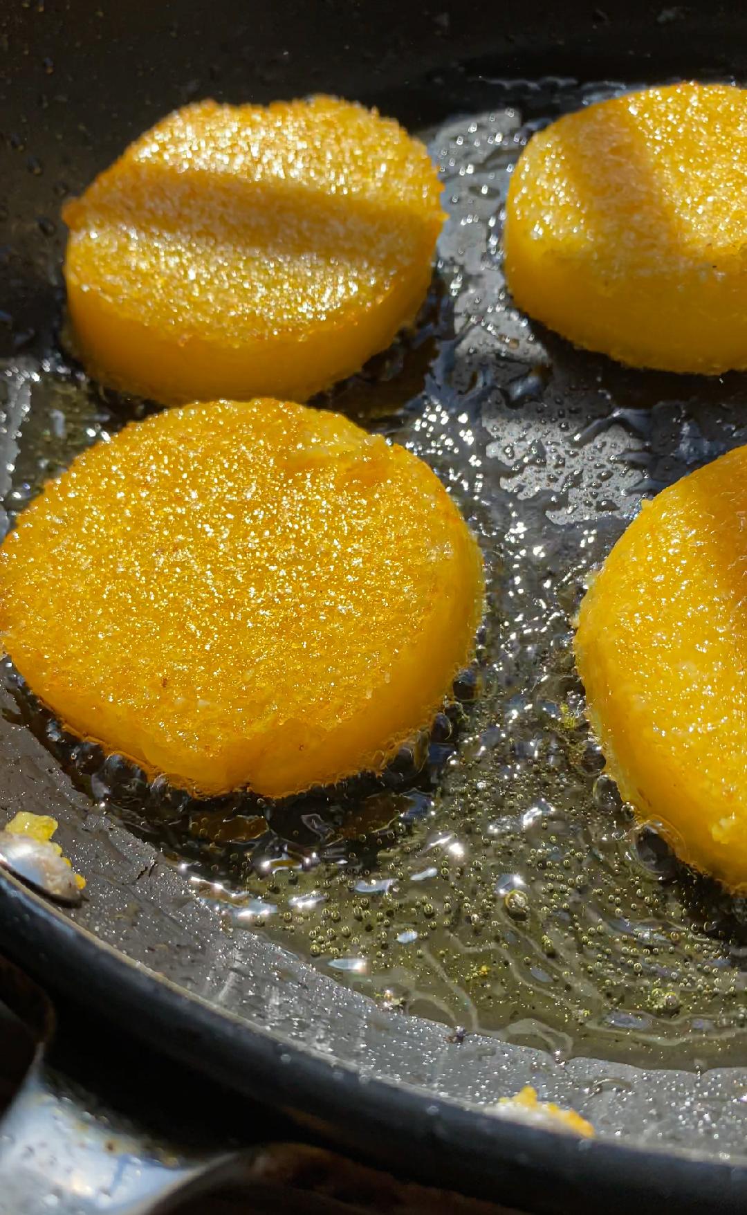 golden crispy polenta rounds being fried in oil in a non-stick pan